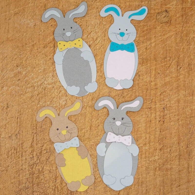 Vier Papier-Osterhasen mit Fliege in bunten Farben, arrangiert auf Holz - ideal zum Basteln zu Ostern mit der Stanzschablone "Süßer Osterhase" von Stanzenshop.de.