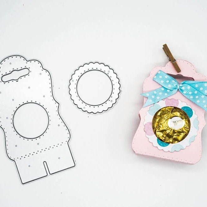 Die Stanzschablone Tischkarte mit Kreis von Stanzenshop.de ist mit einem fertigen rosa Geschenkkarton, einer blauen Tupfenschleife und in Gold verpackten Süßigkeiten abgebildet - ideal für Scrapbooking oder jedes Bastelset-Projekt.