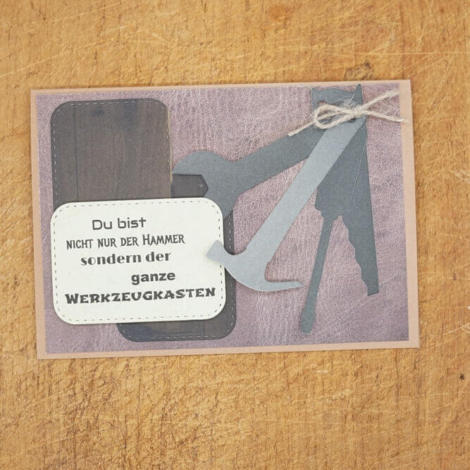 Grußkarte mit der Stanzschablone Vier Werkzeuge von Stanzenshop.de auf Holz, mit Werkzeugsilhouetten und einer deutschen Botschaft: "Du bist nicht nur der Hammer, sondern der ganze Werkzeugkasten." Ideal zum Basteln oder Scrapbooking.