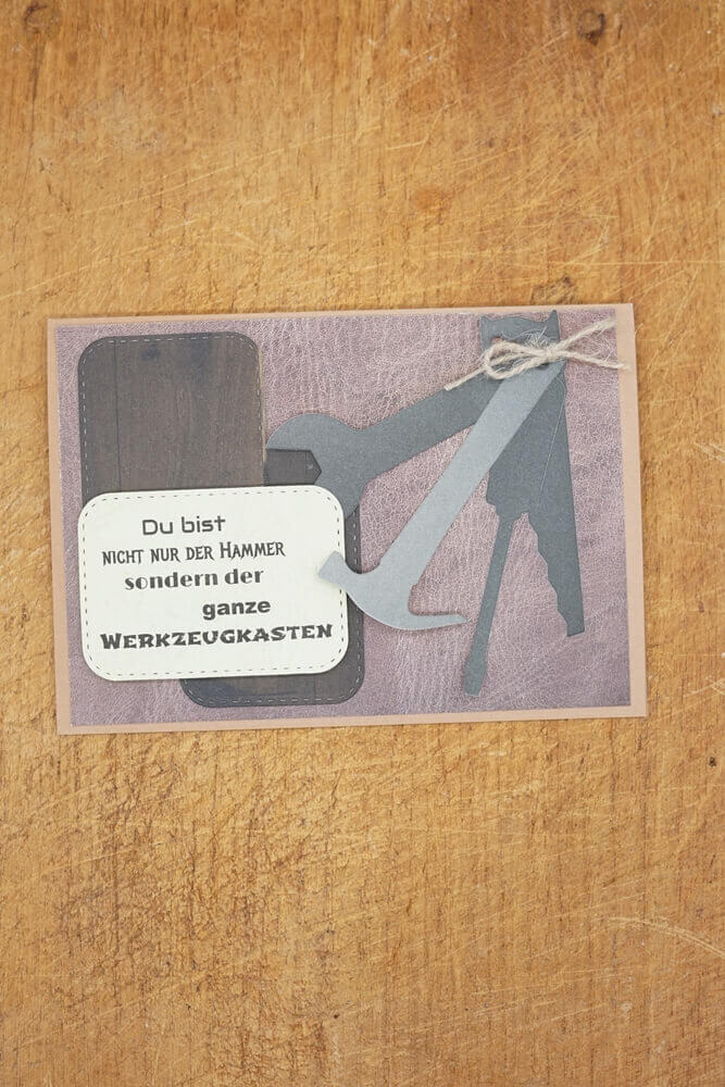 Grußkarte mit der Stanzschablone Vier Werkzeuge von Stanzenshop.de auf Holz, mit Werkzeugsilhouetten und einer deutschen Botschaft: "Du bist nicht nur der Hammer, sondern der ganze Werkzeugkasten." Ideal zum Basteln oder Scrapbooking.