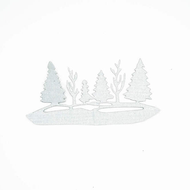 Ein silberner Metallausschnitt, hergestellt mit der Stanzschablone: Waldlandschaft im Winter von Stanzenshop.de zeigt Tannen und kahle Bäume auf einem kleinen Bodenfleck vor einem schlichten weißen Hintergrund.