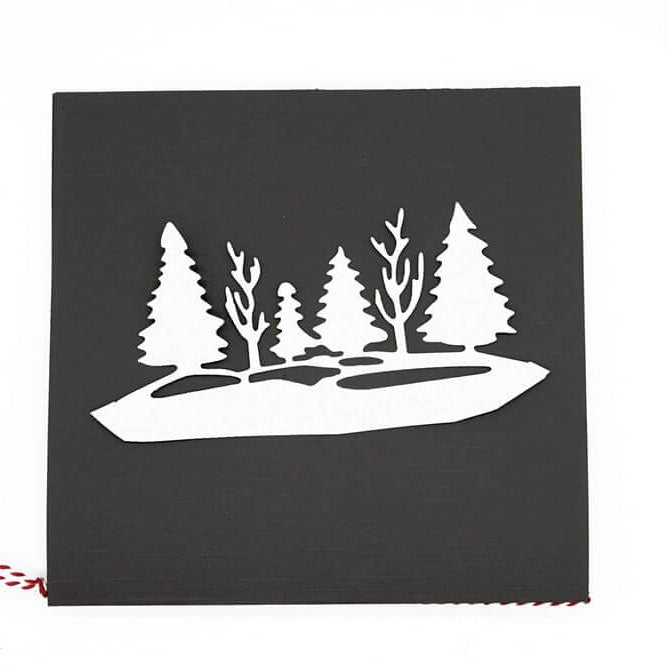 Eine schwarze quadratische Karte zeigt einen weißen Ausschnitt von Tannen und kahlen Bäumen, hergestellt mit der "Stanzschablone: Waldlandschaft im Winter" von Stanzenshop.de. Eine rot-weiße Kordel akzentuiert den linken Rand und sorgt für festlichen Charme.