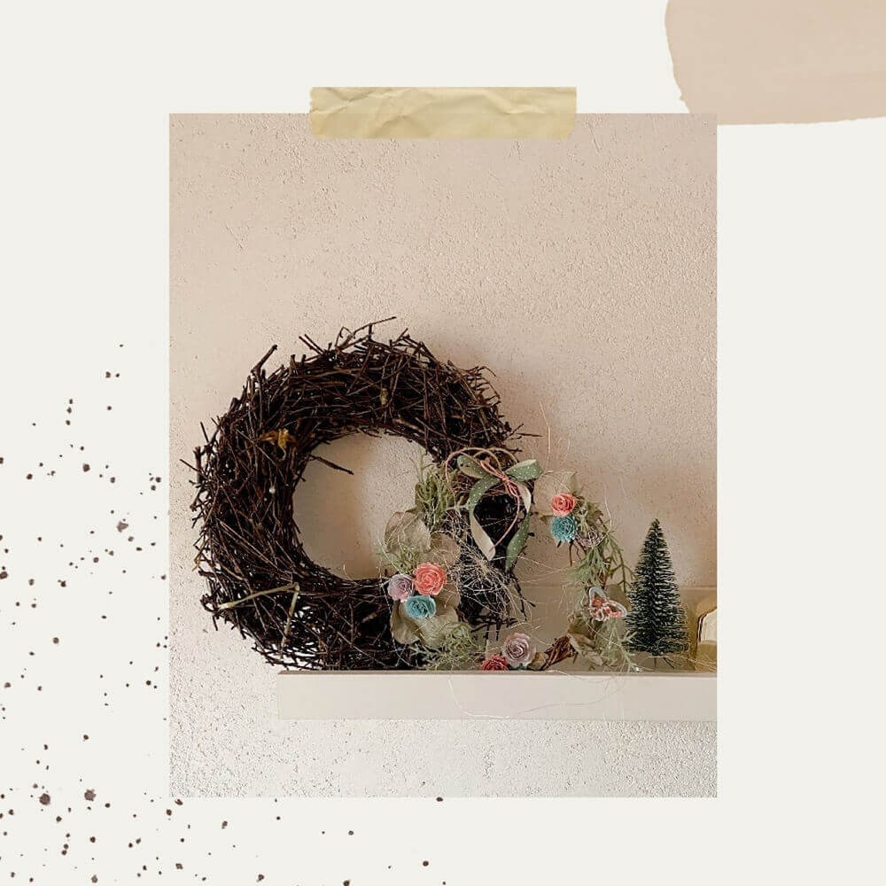 Auf einem dekorativen Regal stehen ein Zweigkranz, ein herzförmiges Ornament mit pastellfarbener Stanzschablone Rosenblüte von Stanzenshop.de und ein kleiner grüner Flaschenbürstenbaum - perfekt, um jeder schlichten Wand Scrapbooking-Charme zu verleihen.