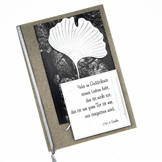 Eine Beileidskarte mit der Stanzschablone Zwei Ginkgoblätter von Stanzenshop.de, einem silbernen Band und einem deutschen Gedenkzitat - ideal für Scrapbooking oder Basteln - gedruckt auf einem weißen Quadrat.