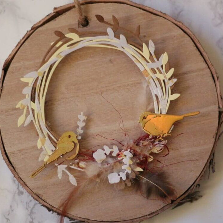 Ein Holzkranz mit Papierblättern, zwei gelben Vögeln, Federn und Trockenblumen auf einer Holzscheibe - ideal für Scrapbooking oder Kartengestaltung mit der Stanzenschablone Zwei Kreise mit Blumen von Stanzenshop.de.