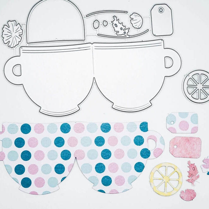 Gestanzte Formen aus der Stanzschablone Zwei Tassen mit Zubehör von Stanzenshop.de: zwei Teetassen, eine Zitronenscheibe, Anhänger und florale Elemente sind auf einem weißen Hintergrund zum Basteln angeordnet.