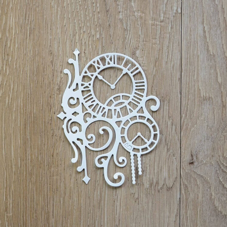Weiße dekorative Uhrenzahnräder und Schnörkel, die mit der Stanzschablone Zwei Uhren mit Ranken von Stanzenshop.de gefertigt wurden, werden auf einer hellbraunen Holzoberfläche dargestellt und bilden ein inspirierendes Bastelergebnis, das sich ideal für Scrapbooking-Projekte eignet.