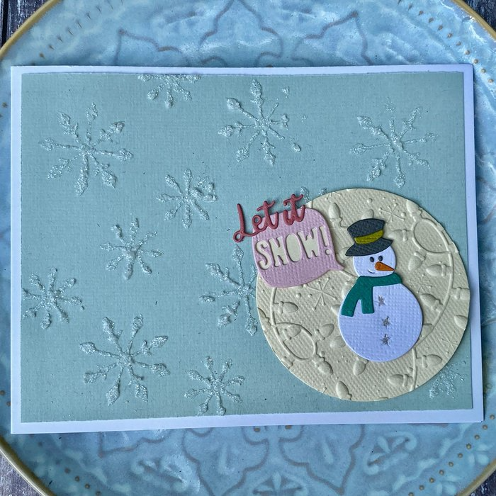 Gestalten Sie festliche Weihnachtskarten mit den Sizzix 665705 - Thinlits Stanzschablonen Weihnachtsfreude von Sizzix, mit strukturierten Schneeflocken und einem Schneemann aus Papier, der ein "Let it Snow!"-Schild hält - in perfekter Größe zum einfachen Verschenken.
