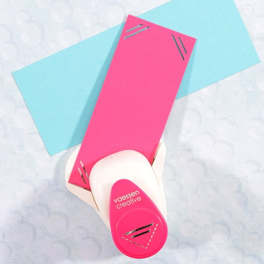 Der Vaessen Creative - Foto Eckenstanzer Recht von Vaessen Creative macht dekorative Eckenschnitte auf rosa und blauem Papier - ideal für Scrapbooking oder zum Anbringen von Fotos.