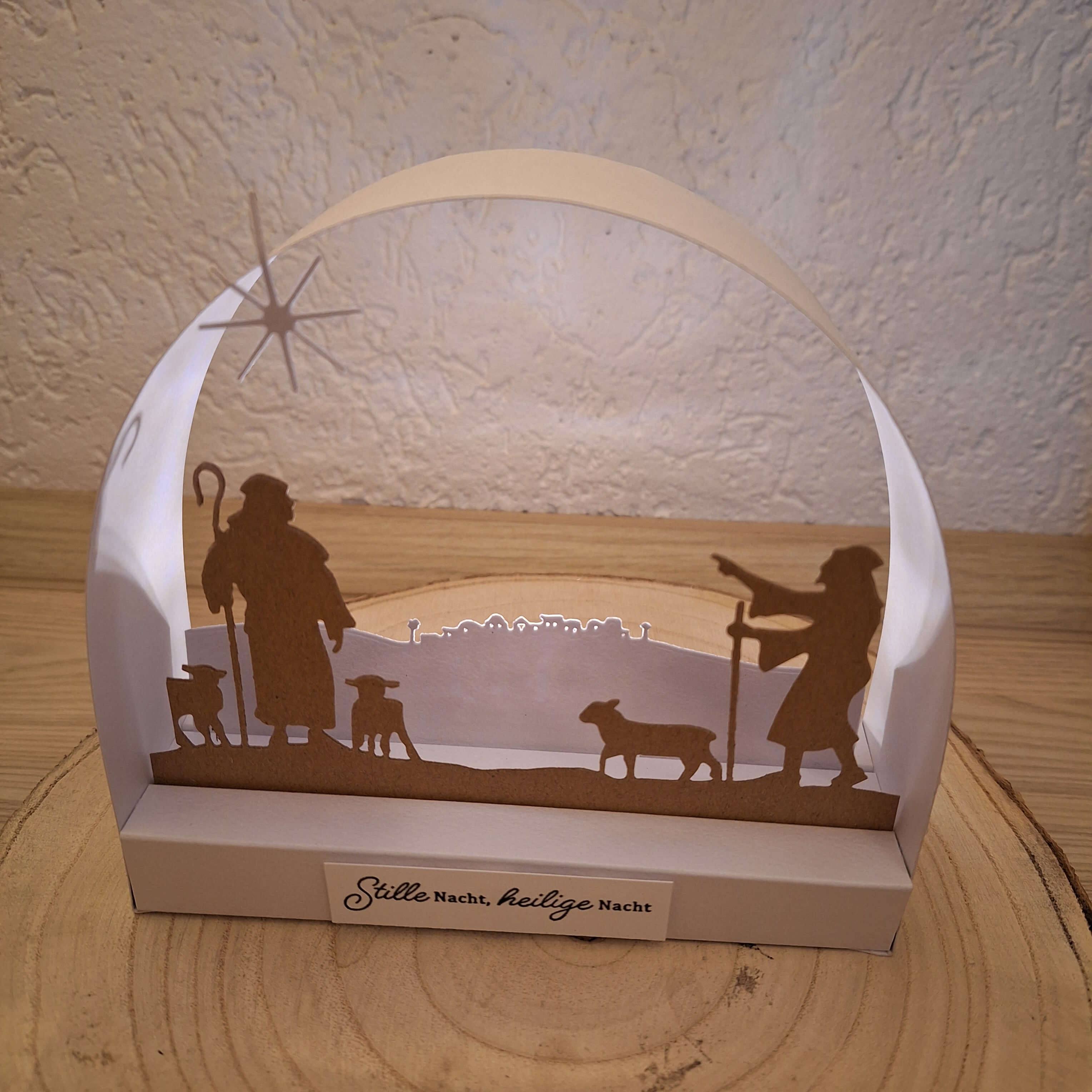 Eine Papierkrippe aus Stanzschablone Hirten von Stanzenshop.de zeigt zwei Hirten, drei Schafe und einen Stern auf Holz. Der Sockel ist mit "Stille Nacht, Heilige Nacht" beschriftet.