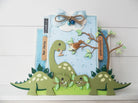 Handgefertigte Karte mit Marianne Design - Collectables Präge- und Stanzschablone Eline's Dinosaurier von Marianne Design, mit Cartoon-Dinosauriern, Blättern, Baum, Vogel, Wolke mit Schleife und Glöckchen; inklusive holländischen Grußanhängern. Ideal für Scrapbooking und Stanzmaschinen.
