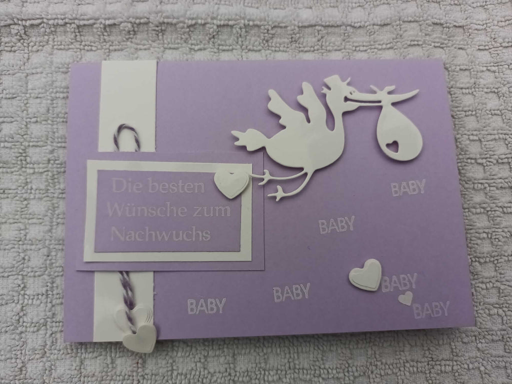 Stanzschablone Storch mit Beutel im Schnabel von Stanzenshop.de, verziert mit Herzen und dem Wort „Baby“ auf Deutsch. Es gibt eine Nachricht auf Deutsch, die übersetzt „Alles Gute für das Neugeborene“ bedeutet. Perfekt für Scrapbooking und kompatibel mit Stanzmaschinen.