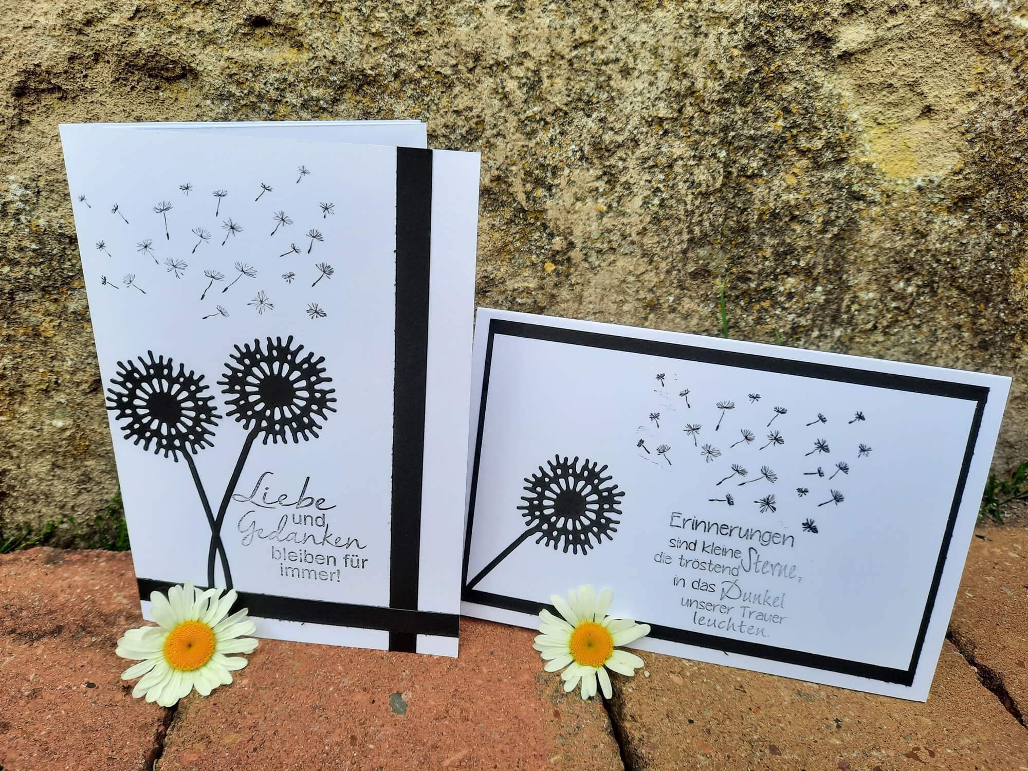 Zwei schwarz-weiße Grußkarten mit Löwenzahn-Motiven aus der "Stanzschablone: Zwei Löwenzahn Pflanzen" von Stanzenshop.de und deutschem Text stehen aufrecht an einer Wand, ideal für Scrapbooking oder Bastelprojekte.