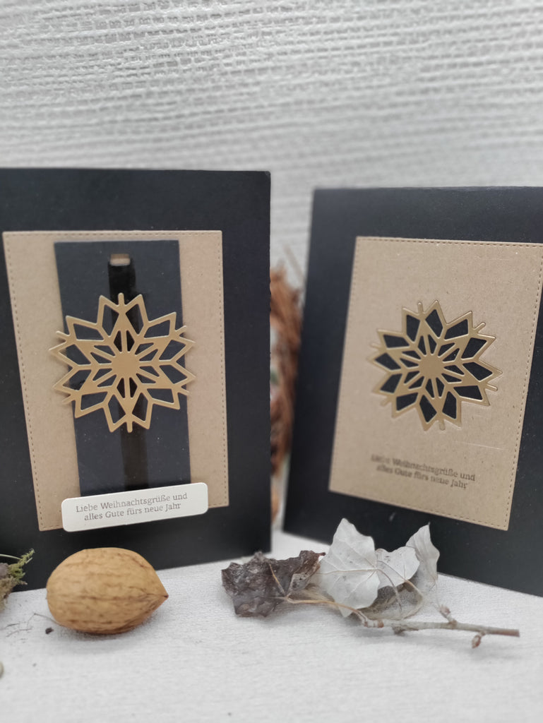 Zwei Grußkarten mit Schneeflockenmotiv in Gold, präzise gefertigt mit Stanzschablone: Schneekristall von Stanzenshop.de. Auf der Vorderseite steht „Liebe Weihnachtsgrüße und alles Gute fürs neue Jahr“. Natürliche Elemente wie Blätter und eine Walnuss stehen im Vordergrund und vervollständigen das Wintermotiv.