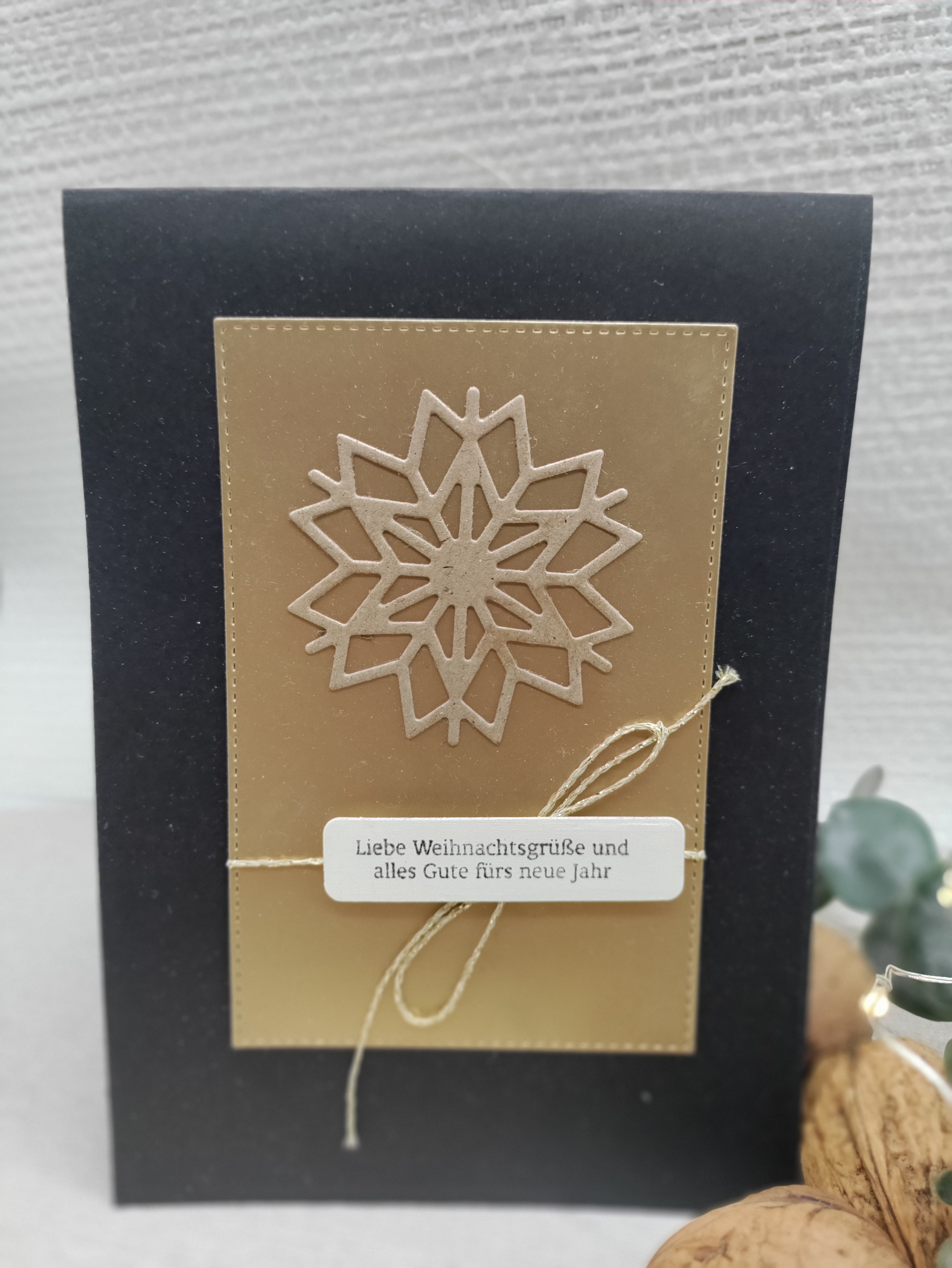 Eine schwarz-goldene Weihnachtskarte mit einer großen Schneeflocke, die mit der Stanzschablone ausgeschnitten wurde: Schneekristall von Stanzenshop.de und einem deutschen Weihnachtsgruß-Etikett, das mit einer goldenen Schnur gebunden ist.