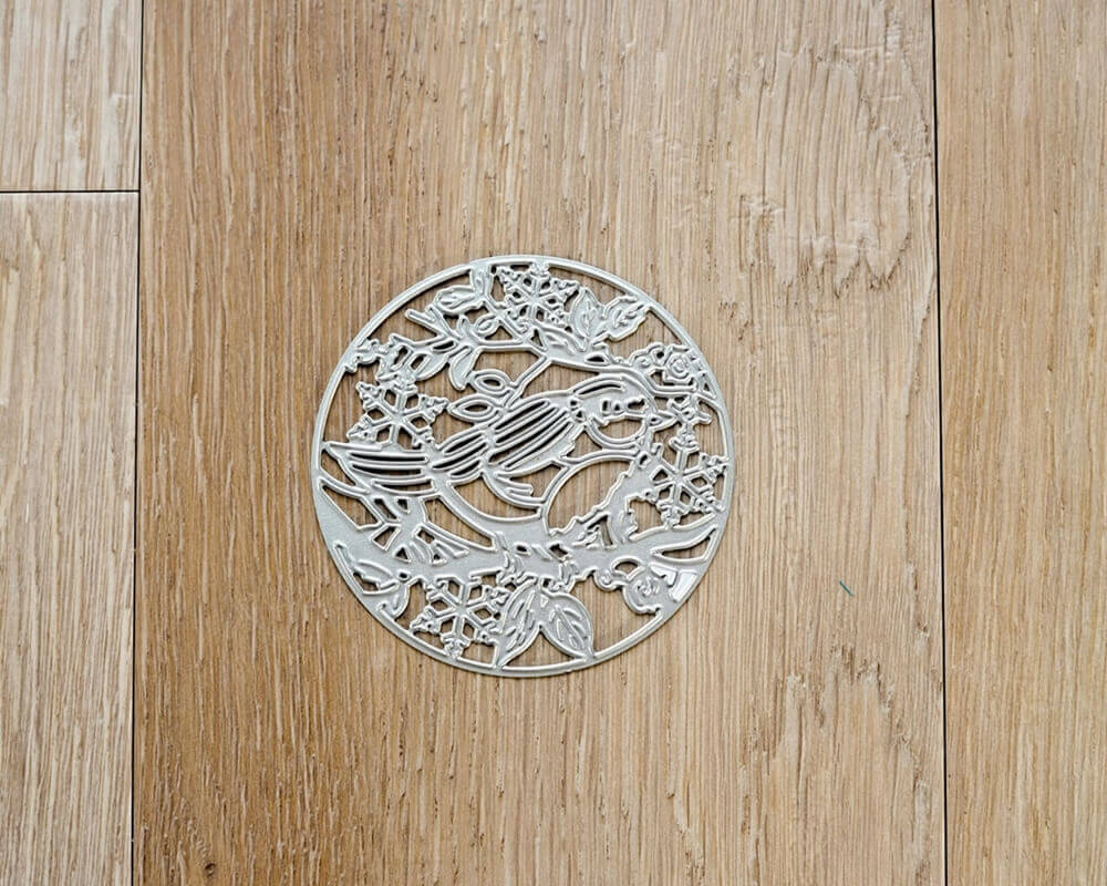 Aufwendiges Kunstwerk aus Metall in Form eines Lebensbaums, eine Stanzschablone: Vogel mit Ästen in einem Kreis von Stanzenshop.de, auf einem Holzboden liegend.