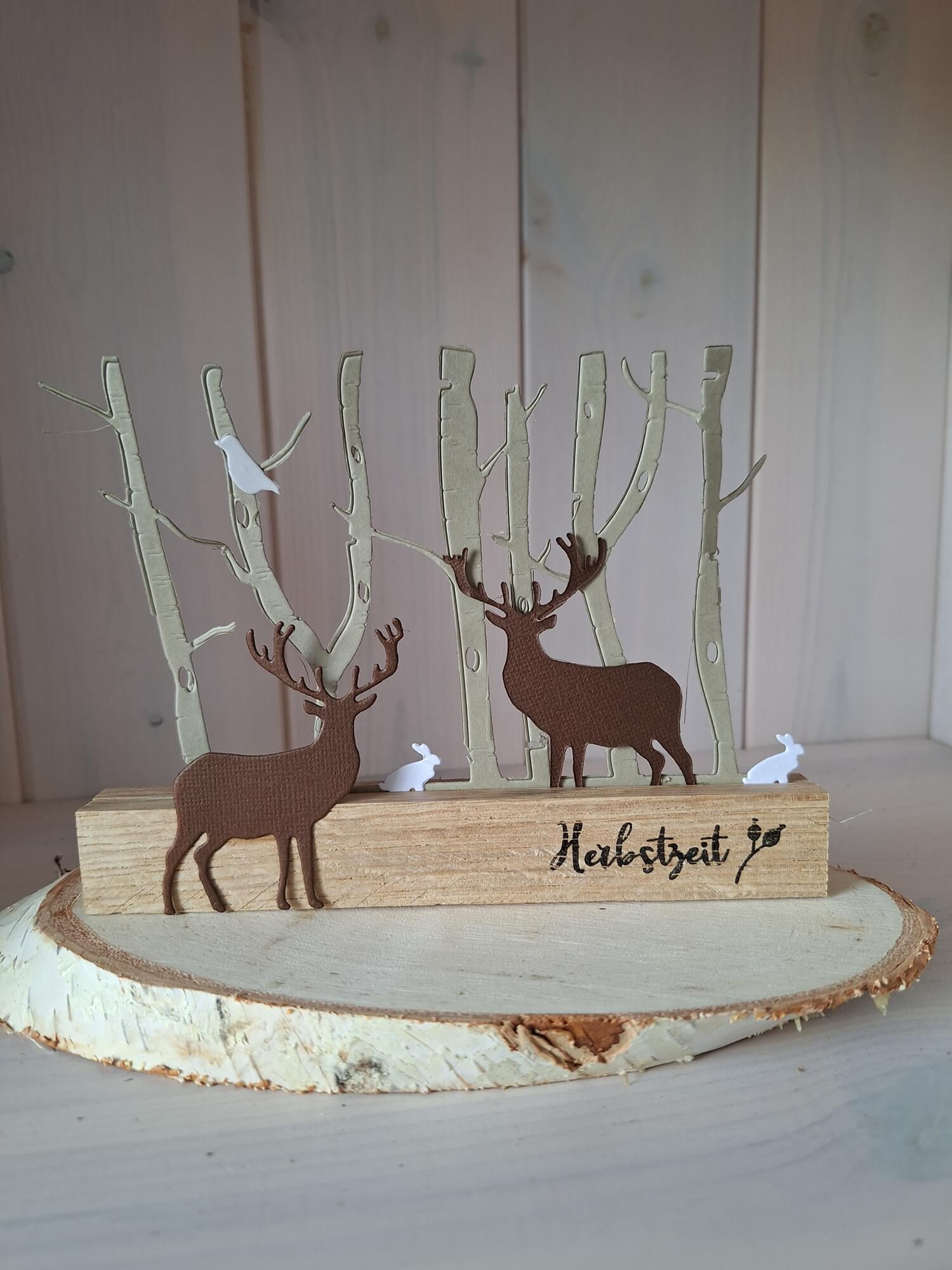 Die "Stanzschablone Wald mit Tieren" von Stanzenshop.de ist eine charmante Holzdekoration mit Rehen, kahlen Bäumen und kleinen weißen Tieren auf einem Holzsockel - perfekt für Scrapbooking oder als Vorlage für kreative Projekte.