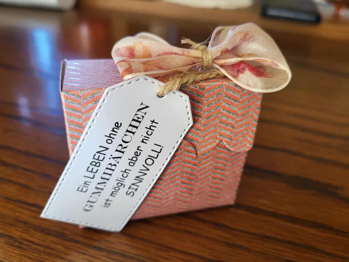 Die "Stanzschablone Schilder in fünf verschiedenen Größen" von Stanzenshop.de liegt auf Holz - ideal zum Basteln oder Scrapbooking, mit rosa Muster, Schleife und einem weißen Etikett mit deutschem Text.