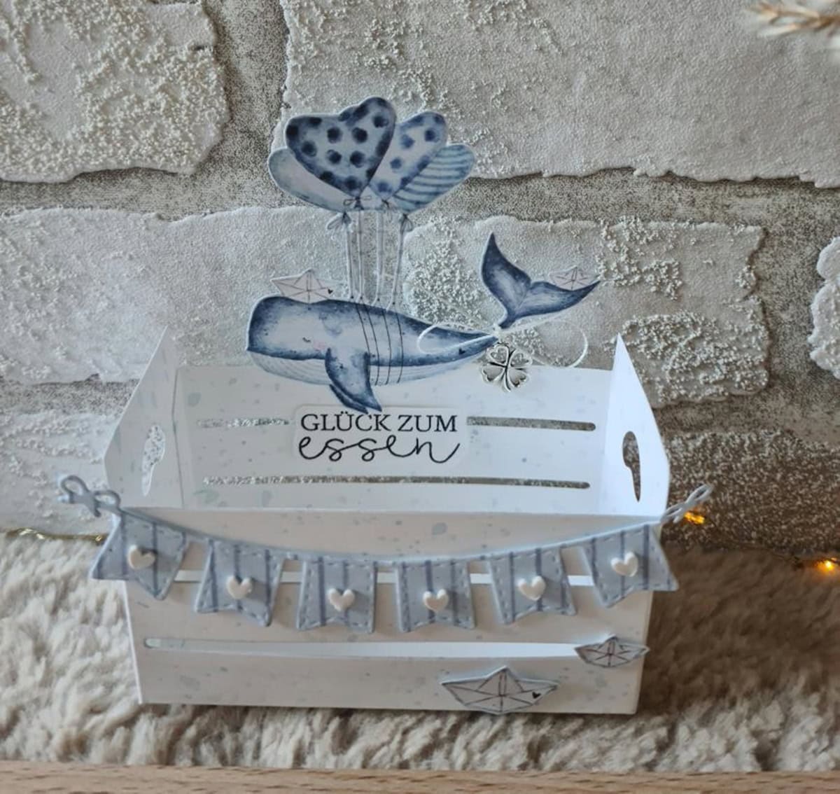 Die "Stanzschablone Vier verschiedene Wimpelketten" von Stanzenshop.de ist eine dekorative weiße Box zum Scrapbooking oder Basteln, mit Wal, Herzluftballons, Papierschiffchen, Girlande und "Glück zum Essen" auf strukturiertem Hintergrund.