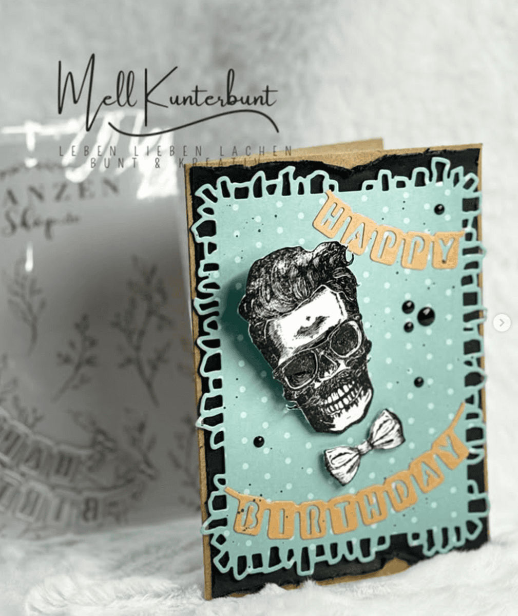 Für die handgefertigte Geburtstagskarte wurde die Stanzschablone Wimpelkette Happy Birthday von Stanzenshop.de verwendet. Sie zeigt einen Totenkopf mit gestyltem Haar und Fliege auf blauem Hintergrund, mit aufwendigen Cut-Outs und festlichen "Happy Birthday"-Akzenten.