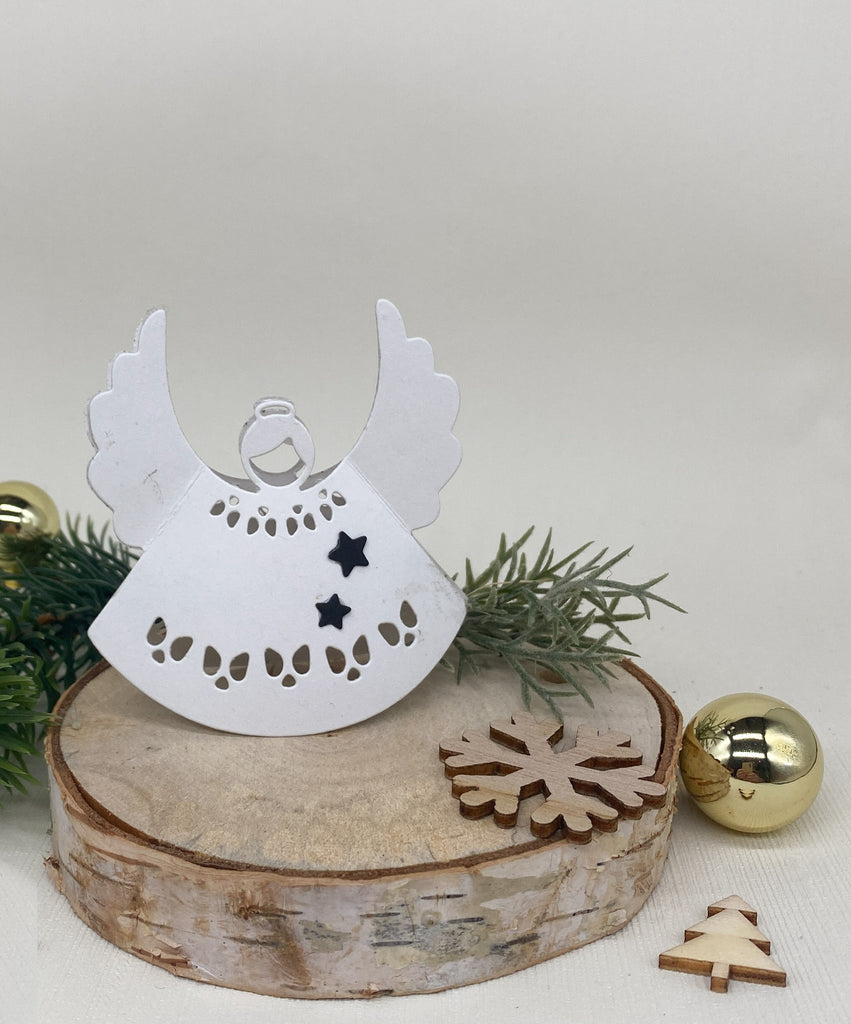 Eine weiße Engeldekoration aus Papier, hergestellt mithilfe einer Stanzschablone: Engel von Stanzenshop.de mit Sternen, wird auf eine Holzscheibe gesetzt, begleitet von einer kleinen hölzernen Schneeflocke, einem ausgeschnittenen Weihnachtsbaum, Grünzeug und einem goldenen Ornament.