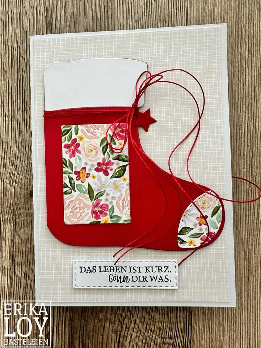 Handgefertigte Grußkarte mit einem roten Weihnachtsstrumpf, hergestellt mit Stanzschablone: Stiefelumschlag von Stanzenshop.de und floralen Motiven. Perfekt für Bastelprojekte Weihnachten. Inklusive roter Schnur und Anhänger: "DAS LEBEN IST KURZ. GÖNN DIR WAS.