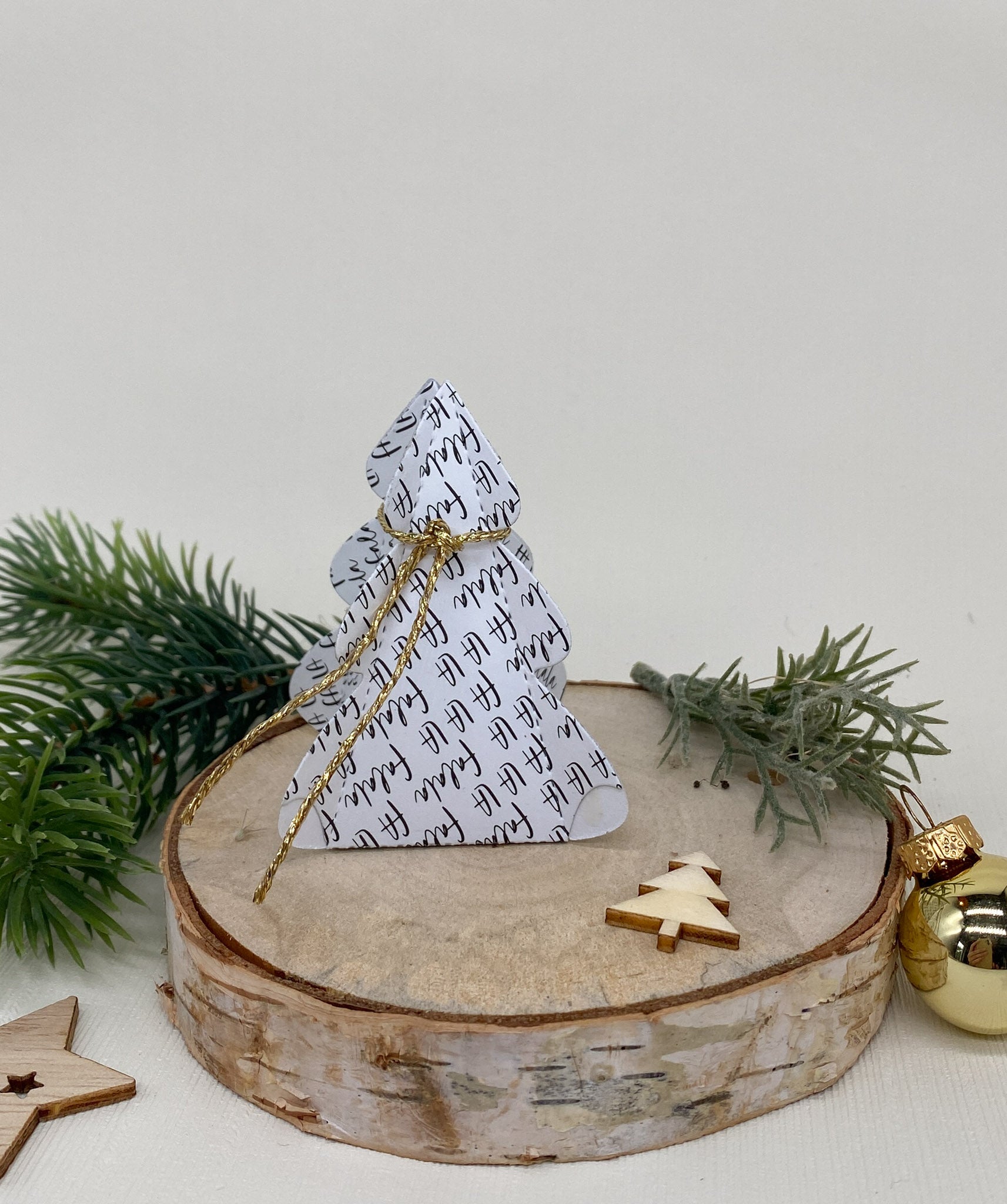 Die Stanzschablone: Tannenbaumschachtel von Stanzenshop.de bildet eine einzigartige Weihnachtsbaumschachtel, ideal für kreative Geschenkverpackungen, die mit festlichem Grün und Ornamenten auf Holz präsentiert werden.