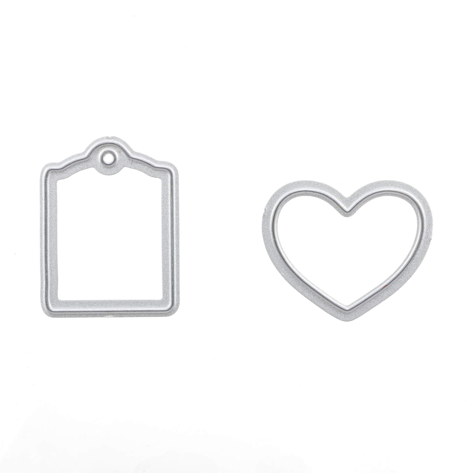 Die Stanzschablone: Tassen von Stanzenshop.de ist ein silberner rechteckiger Anhänger mit einem Loch oben links und herzförmigem Umriss, perfekt als Bastelzubehör für kreative Projekte oder als Tassenstanze, abgebildet auf weißem Hintergrund.
