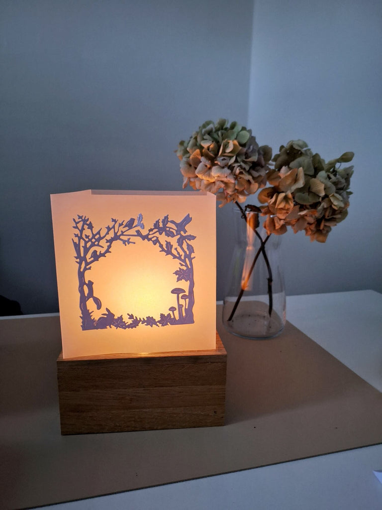 Beleuchtete Papierschnitt-Stanzschablone von Stanzenshop.de: Herbstwaldlampe neben einer Vase mit getrockneten Hortensien.