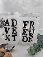 Zwei weiße Laternen mit schwarzen Buchstaben "ADVENT" und "FREUDE", geschnitten mit Stanzschablone: Blumenalphabet von Stanzenshop.de, umrahmt von Walnüssen, Blättern und Grünzeug - ideal für personalisierte Botschaften in Ihrer Einrichtung.
