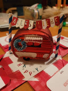 Ein rotes Ornament in Form einer Karawane mit Kranz und Schnee sitzt unter einem "ALLES LIEBE"-Banner. Für die Szene wurde die "Stanzschablone" von Stanzenshop.de verwendet: Wimpelkette mit Buchstaben", ideal für persönliche Kartendekorationen und Botschaften.