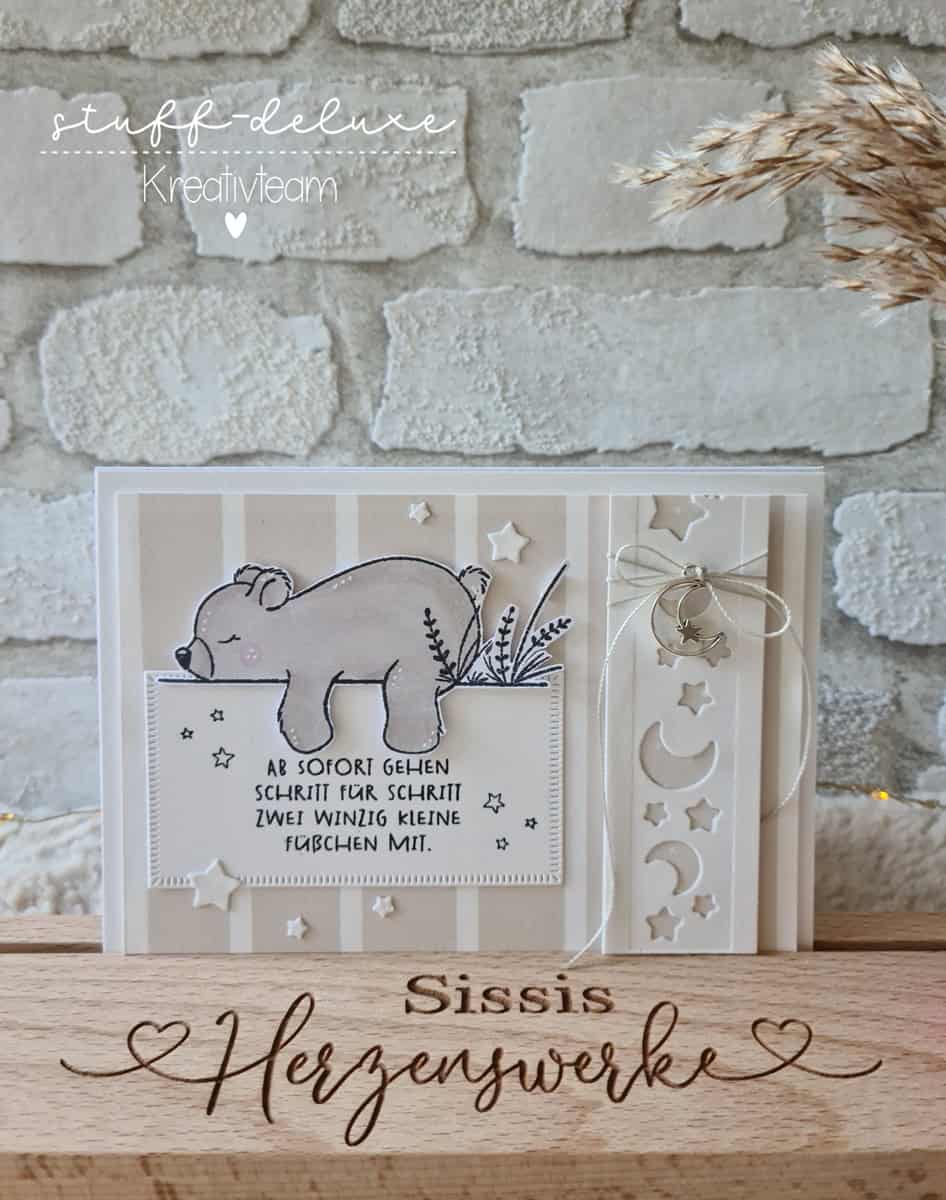 Die "Stanzschablone: Mond /Sterneband" von Stanzenshop.de ist mit Mond- und Sternenmotiven versehen und eignet sich perfekt für Bastelprojekte. Abgebildet mit einer handgefertigten Karte mit Bärenmotiv, deutschem Text und dekorativer Kordel vor einer gemütlichen Backsteinmauer-Kulisse.