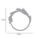 Die Stanzschablone Kranz mit Zweigen von Stanzenshop.de aus silbernem Metall misst 11,3 x 11,5 cm und zeigt filigrane, blattähnliche Zweige - ideal für Bastelprojekte. Darstellung auf weißem Hintergrund mit Maßlinien.