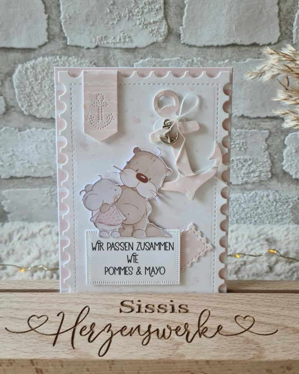 Eine handgefertigte Karte mit Cartoon-Bären, einem Anker und "Wir passen zusammen wie Pommes & Mayo" auf Deutsch, hergestellt mit Scrapbooking und der Stanzschablone Drei Briefmarken von Stanzenshop.de, steht auf einem "Sissis Herzenwerke" Holzblock.