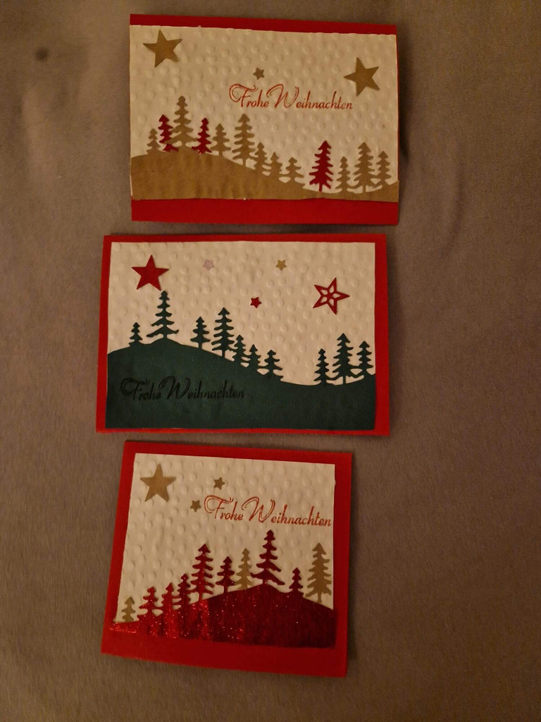 Drei handgefertigte Weihnachtskarten mit „frohe Weihnachten“-Text, festlichen Baummotiven und Stanzschablone: Berglandschaft mit Bäumen-Motiven von Stanzenshop.de.