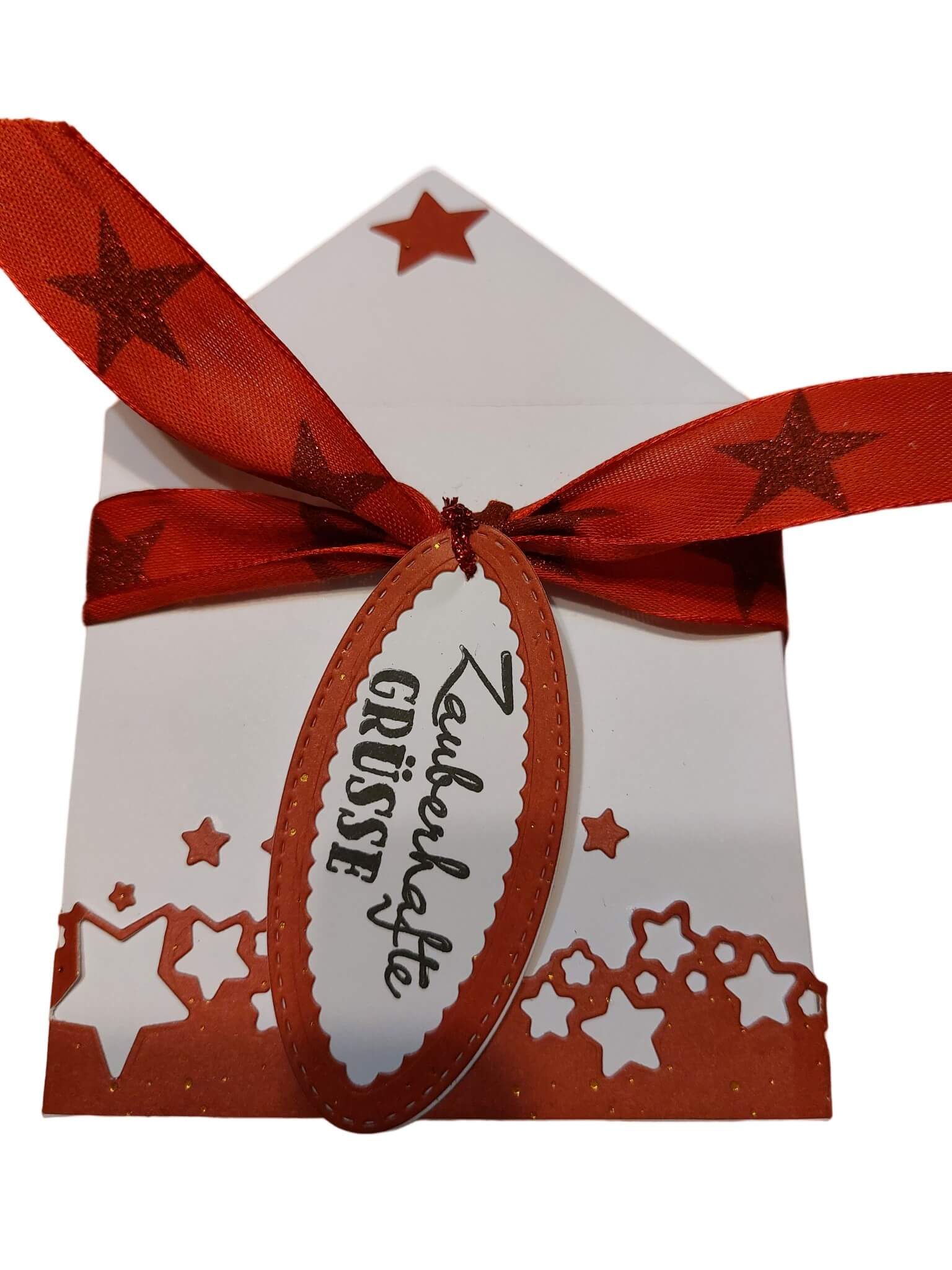 Ein weißer Umschlag mit Sternchenbordüre, rotem Sternchenband und "Zauberhafte Grüße"-Anhänger - ideal zum Karten basteln oder als Wintermotiv mit der Stanzschablone: Sterne auf einer Welle von Stanzenshop.de.