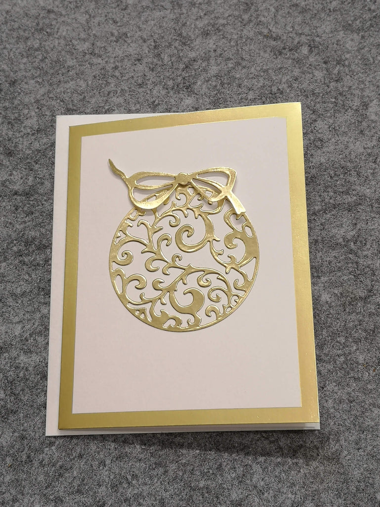 Eine handgefertigte Grußkarte mit goldener dekorativer Stanzschablone: Zwei ausgeschnittene Weihnachtskugeln auf cremefarbenem Hintergrund mit goldenem Rand von Stanzenshop.de.