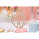 Sizzix 666230 - Thinlits Fabulous Birthday Numbers von Debi Potter Kuchentopper auf rosa Macarons, ideal für das Scrapbooking von Partyerinnerungen. Champagnergläser und eine blaue Geschenkbox erscheinen im verschwommenen Hintergrund. Marke: Sizzix.