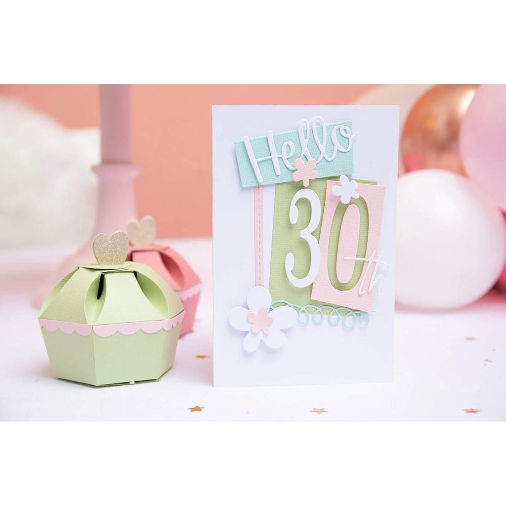 Eine „Hallo 30.“-Grußkarte in Pastellfarben ist neben einer kleinen, dekorativen Schachtel und einigen Luftballons im Hintergrund abgebildet, perfekt für Scrapbooking-Enthusiasten und Kartenherstellungsprojekte, mit dem Sizzix Thinlits Die Set Fabulous Frames & Borders von Debi Potter von Sizzix.