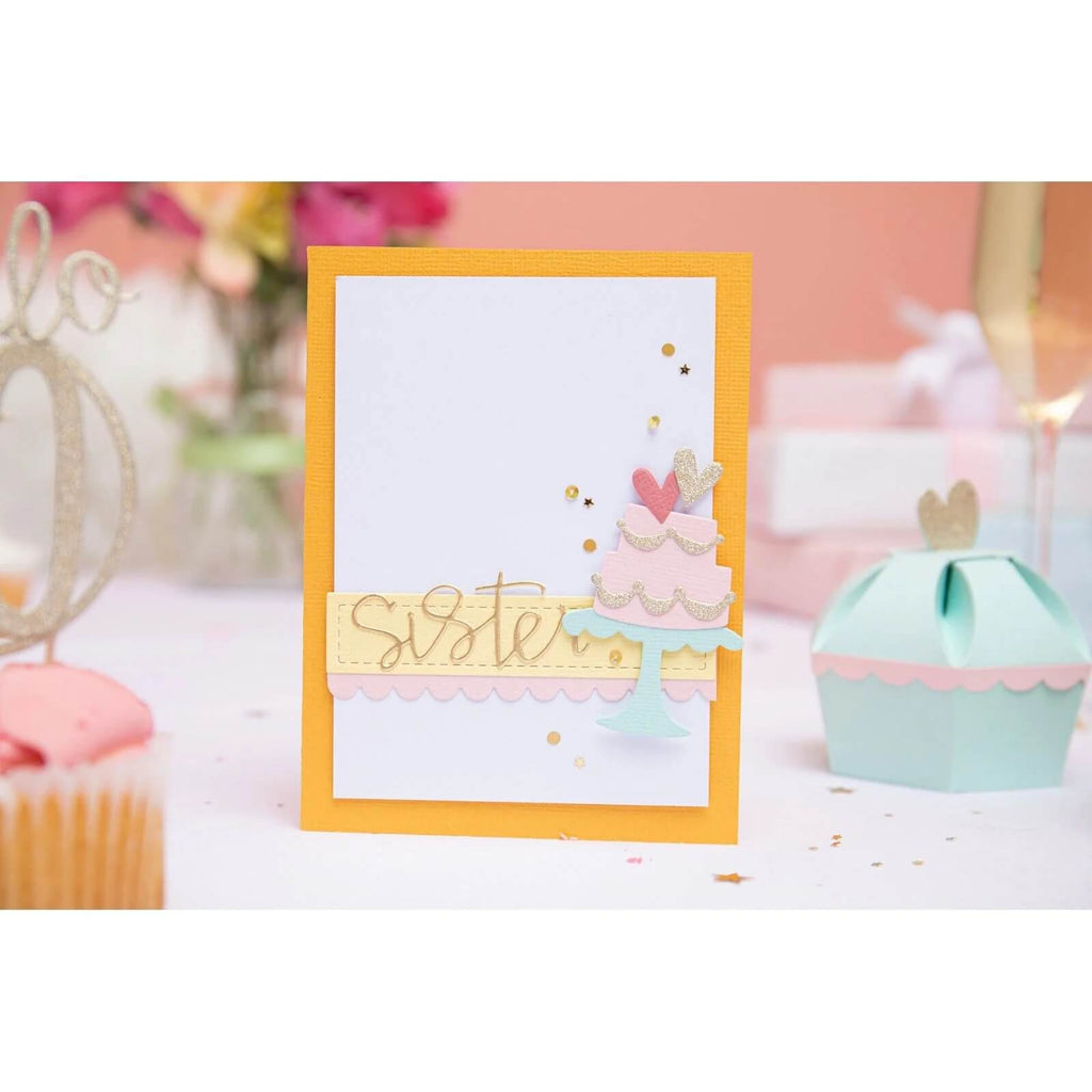 Das Sizzix Thinlits Stanzset Fabulous Frames & Borders von Debi Potter kommt auf einem mit festlichen Dekorationen und einem Cupcake geschmückten Tisch wunderschön zur Geltung. Das aufwendige Stanzdesign mit dem Text „Sister“, einer Kuchenillustration und Herzverzierungen lässt auf fachmännische Kartenherstellungstechniken schließen und ist daher perfekt für Scrapbooking-Fans.