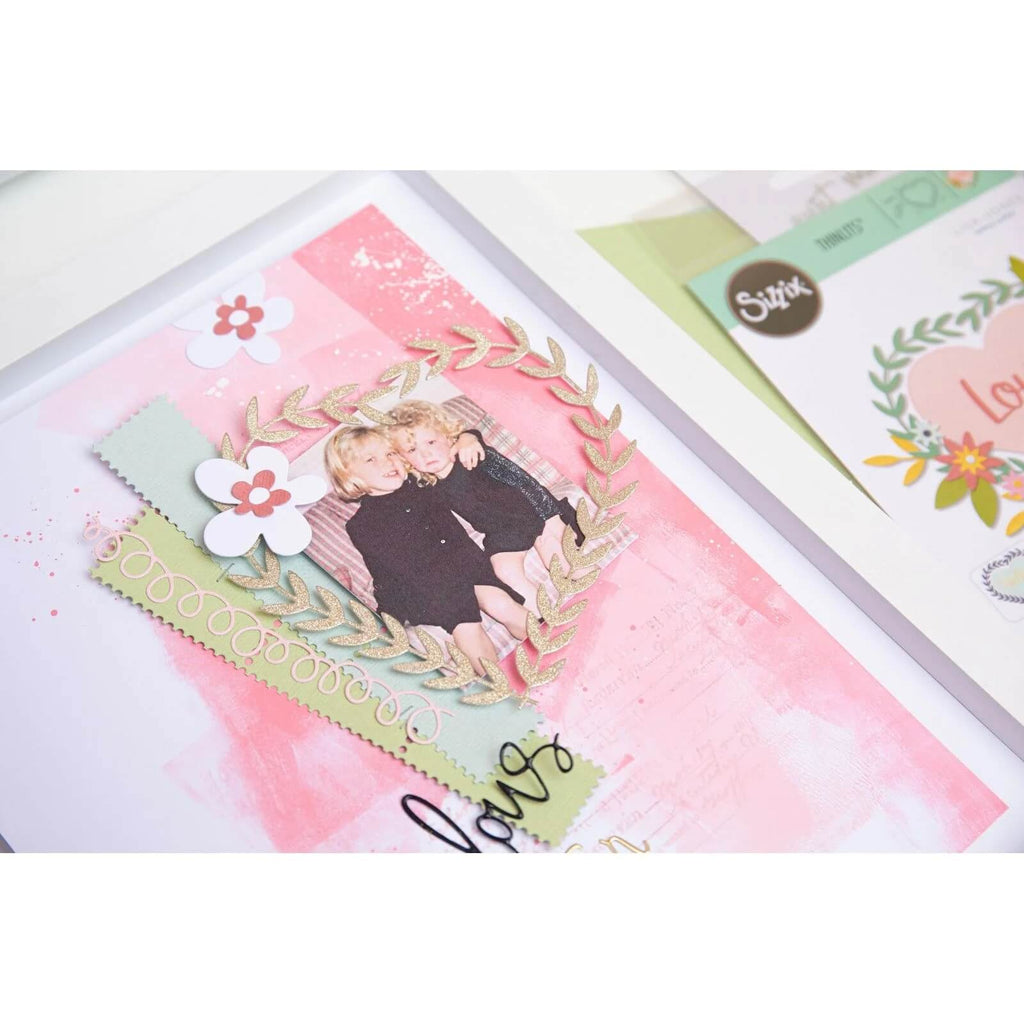 Eine Scrapbook-Seite mit einem Foto von zwei Kindern in einem dekorativen Rahmen. Die Seite ist perfekt für Scrapbooking-Fans und enthält florale Verzierungen, einen rosa Hintergrund und das Wort „Liebe“ in Schreibschrift. Die komplizierten Details dieses charmanten Layouts wurden mit dem Sizzix Thinlits Die Set Fabulous Frames & Borders von Debi Potter hinzugefügt.