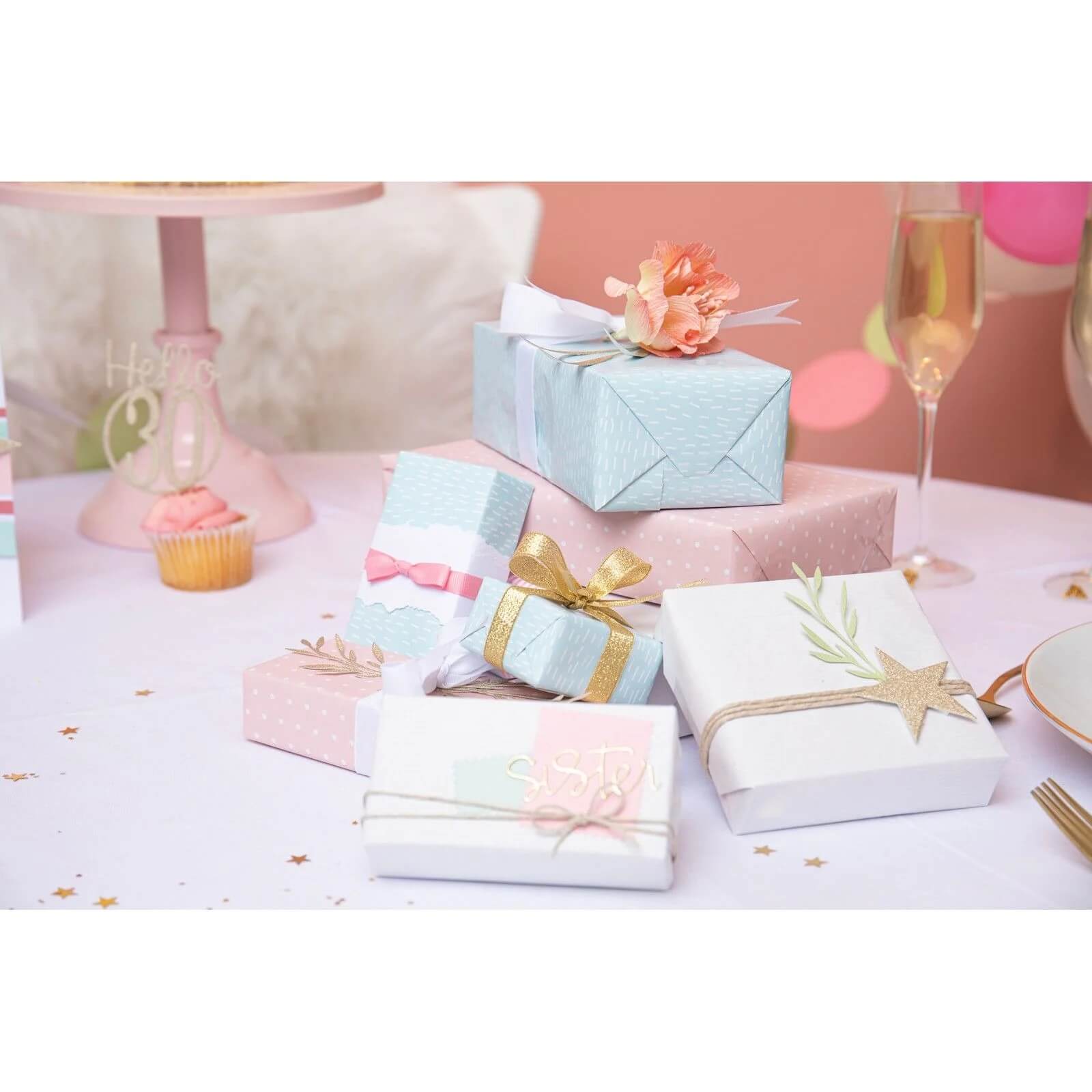 Eine Vielzahl von pastellfarbenen Geschenkboxen mit Bändern, Partyartikeln und einem Glas Champagner werden mit Scrapbooking-Akzenten dargestellt, die mit den Sizzix 666254 - Thinlits Woodland Stems von Olivia Rose für die kreative Kartengestaltung hergestellt wurden.