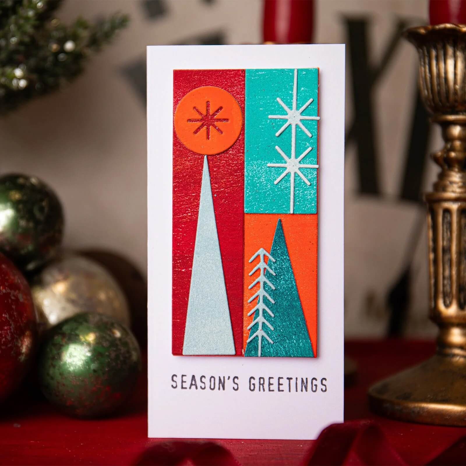 Inspiriert von Weihnachten, zeigt diese Karte geometrische Bäume, Sterne und festliche Akzente in Rot, Grüntönen und Orange. Fertiggestellt mit "Season's Greetings" und den Sizzix 666335 Thinlits Stanzschablonen Holiday Blocks von Sizzix.