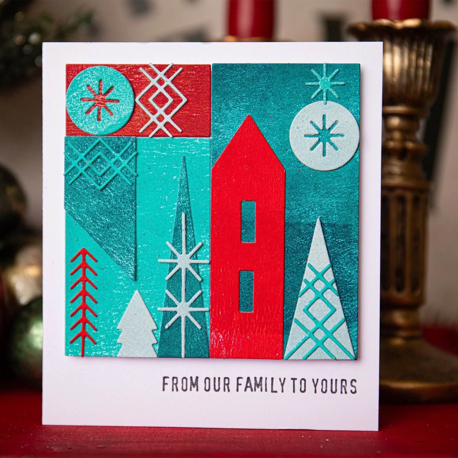 Versenden Sie Weihnachtsstimmung mit einer Karte, die mit den Sizzix 666335 Thinlits Stanzschablonen Holiday Blocks von Sizzix erstellt wurde. Die Karte zeigt geometrische Bäume in Rot, Petrol und Weiß und den Gruß "FROM OUR FAMILY TO YOURS" - perfekt für Weihnachten!.