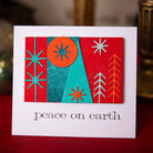 Eine Weihnachtskarte mit geometrischen Formen und Sternenmotiven in Rot, Petrol und Orange, erstellt mit den Sizzix 666335 - Thinlits Stanzschablonen Holiday Blocks von Sizzix, darüber "Friede auf Erden" in Kleinbuchstaben. Ideal für Weihnachtsfeiern.