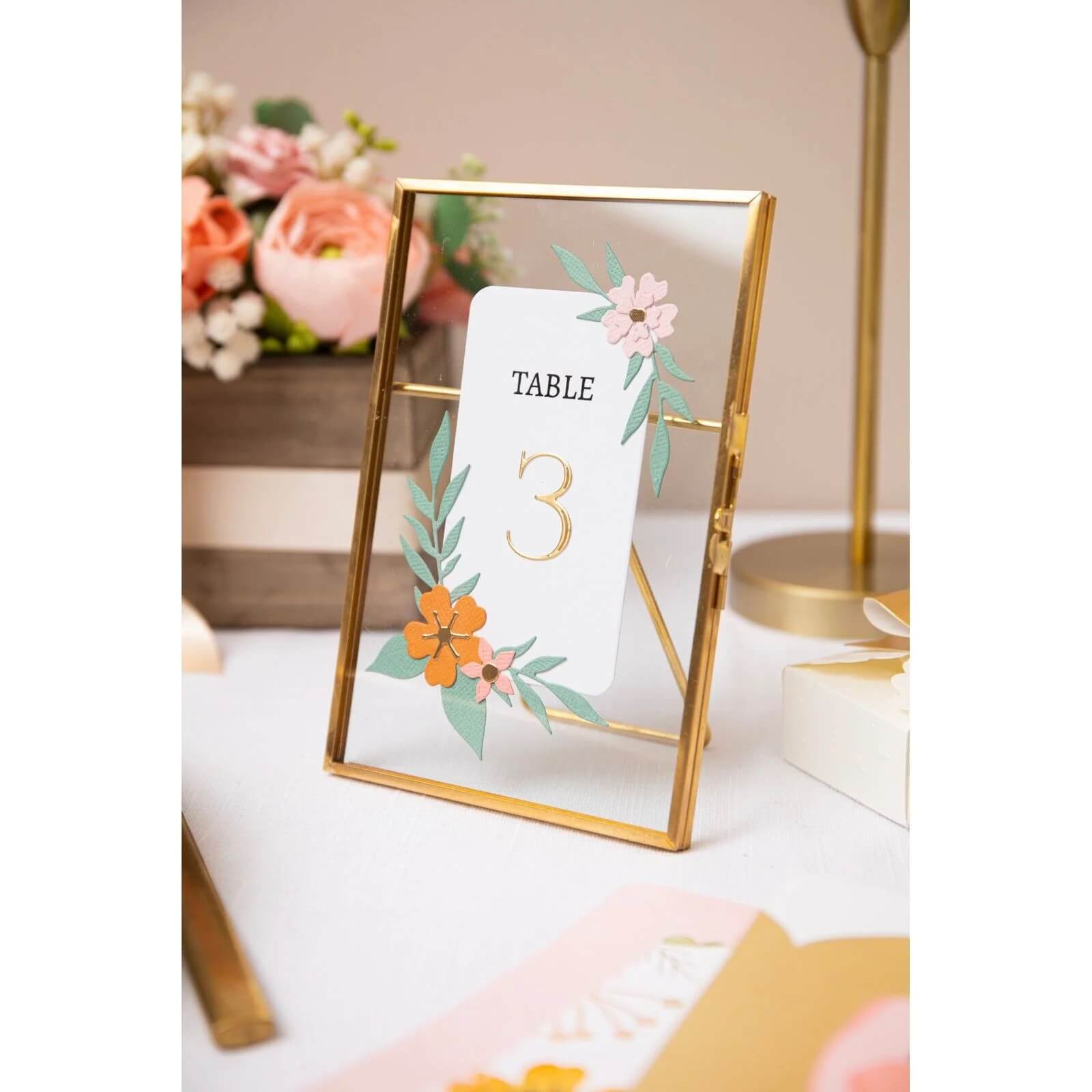 Eine goldgerahmte Tischnummernkarte mit floralen Akzenten lautet "Tisch 3" - ideal für Scrapbooking oder Kartenherstellung mit Sizzix 666444 - Thinlits Die Elegant Numerals von Sizzix.