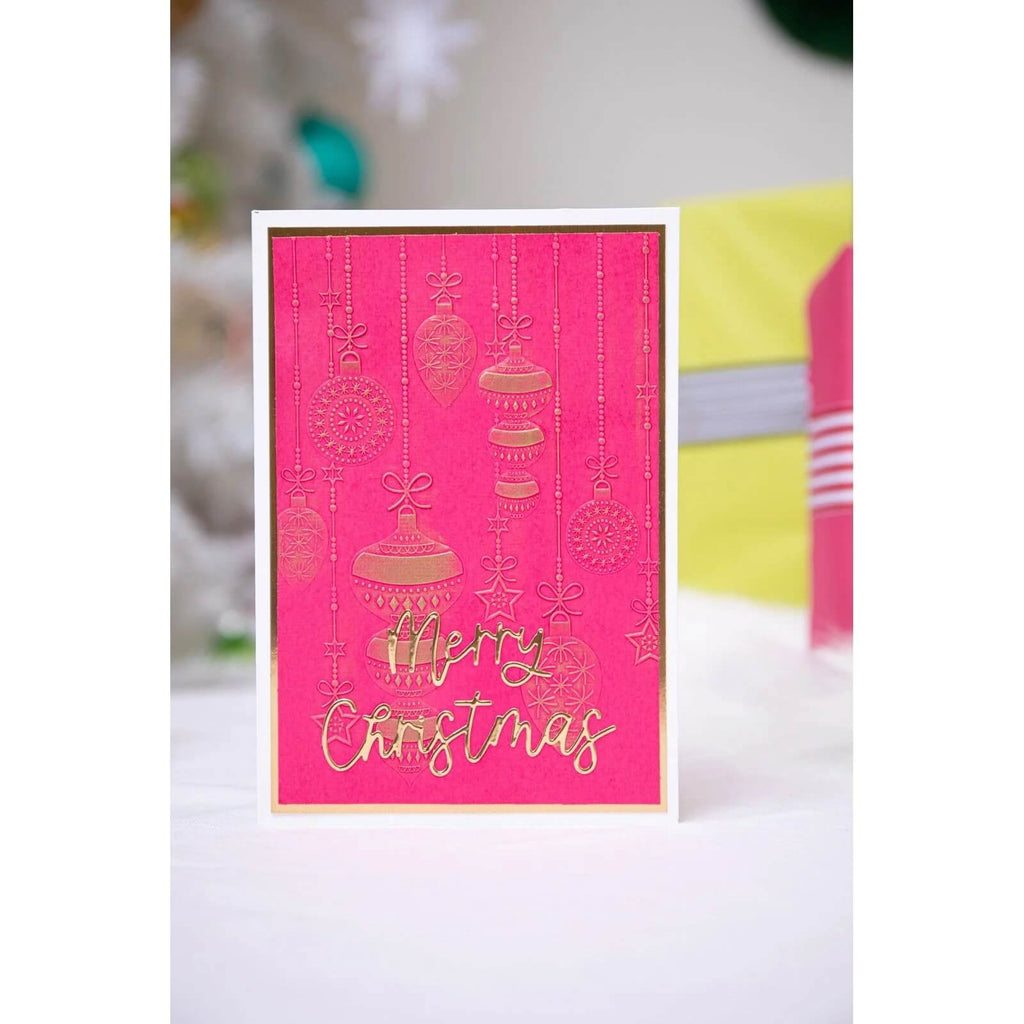 Eine rosa-goldene Sizzix • Thinlits Die Set Variety Sentiments #2 Frohe Weihnachtskarte mit Text auf einem Tisch.