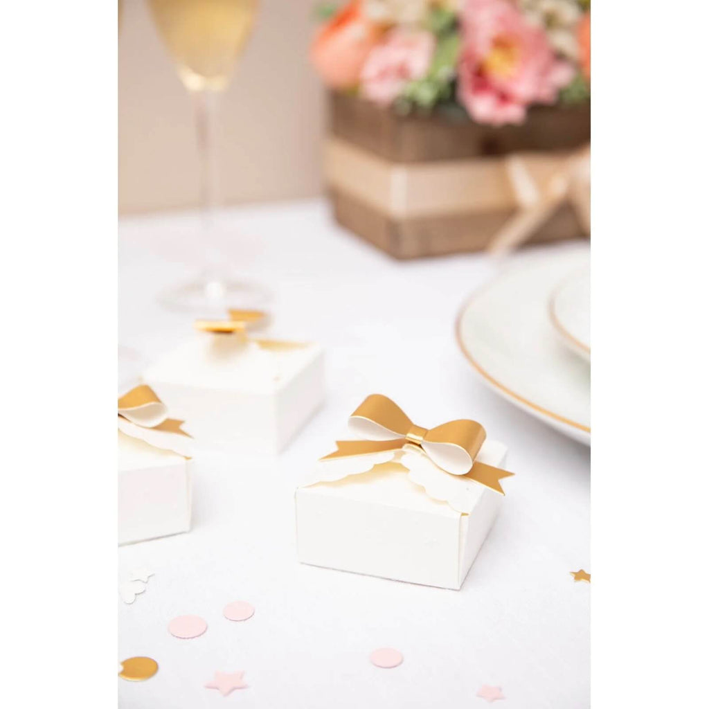 Kleine weiße Sizzix-Boxen mit goldenen Schleifen auf einem Tisch von Jennifer Ogborn.