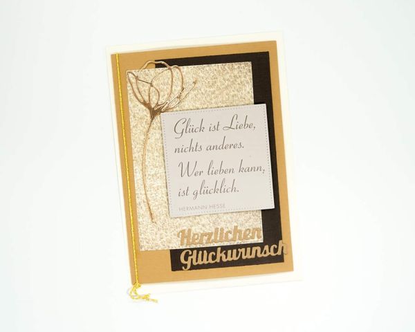 Eine gold-schwarze Karte mit einem Zitat darauf, verziert mit der Dekoration „Stanzschablone Blume mit zwei Blüten“ von Stanzenshop.de.