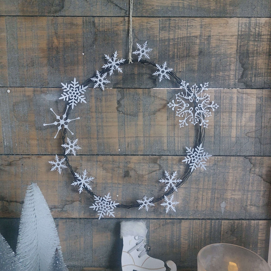 Ein Schneeflockenkranz aus Stanzschablone Vier Schneeflocken in verschiedenen Größen, der an einer Holzwand hängt. (Marke: Stanzenshop.de)